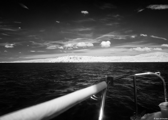 Vue de la poupe.Sur la ligne d'horizon, à gauche, l'Isola Maggiore et la silhouette du château Guglielmi.à droite la forme plus "grossière" de l'Isola Minore.Au-dessus, ce beau ciel avec quelques nuages bien solitaires...10:14.